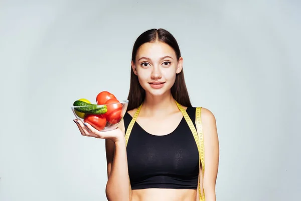 Uma jovem menina bonita em um top preto quer perder peso, segura um prato com vegetais úteis e frutas em suas mãos — Fotografia de Stock