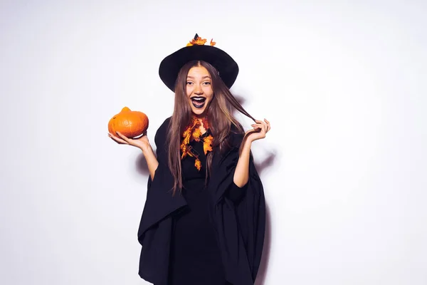Mladá sexy veselá gotická dívka slaví halloween, čarodějnice, velký černý klobouk, držící dýně a směje se na sobě — Stock fotografie