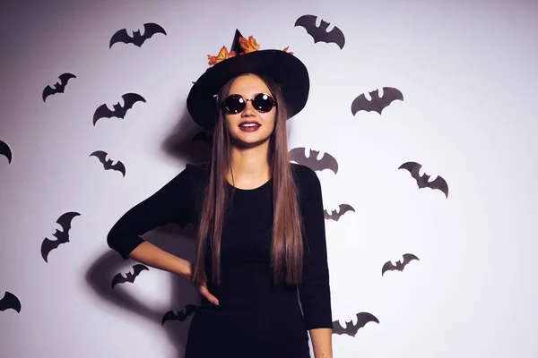 Una joven chica gótica sexy celebra halloween, vestida con una bruja, sobre su cabeza un gran sombrero negro decorado con hojas amarillas de otoño —  Fotos de Stock