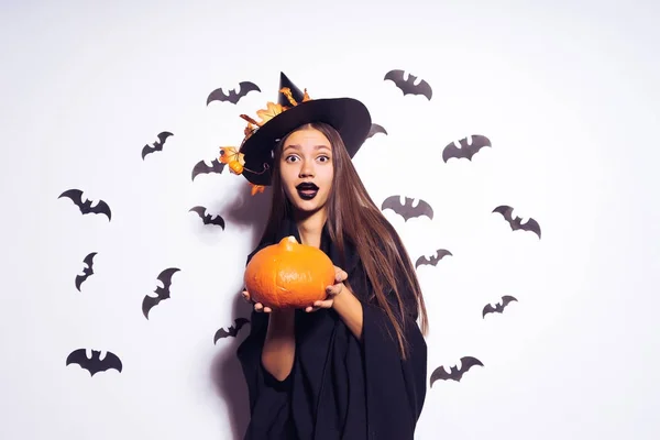 Uma jovem menina gótica sexy celebra halloween, vestida com uma bruxa, segura uma abóbora em suas mãos — Fotografia de Stock