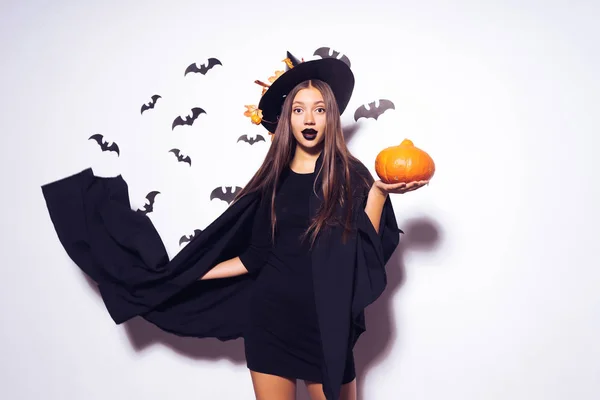 Een jonge sexy gothic meisje viert halloween, gekleed in een heks, houdt een pompoen in haar handen — Stockfoto