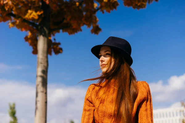 流行のオレンジ色のセーターで美しい赤毛の少女が公園で座っています。 — ストック写真