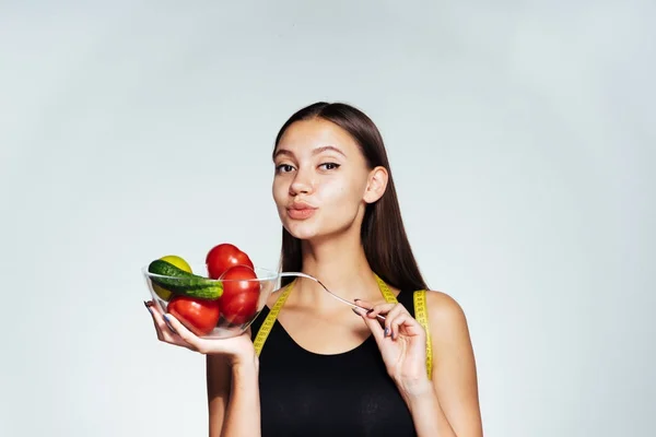 En ung atletisk flicka i en svart topp håller reda på sin figur, innehar en tallrik med användbar grönsaker och frukter i händerna — Stockfoto