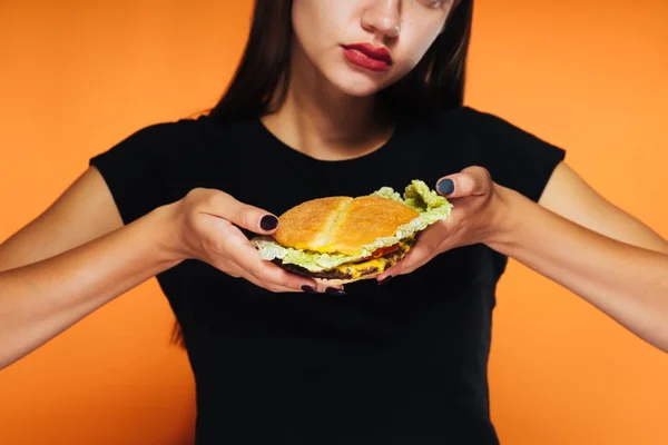 Jovem menina bonita quer perder peso, mas ansiosamente come um hambúrguer prejudicial de alta caloria — Fotografia de Stock