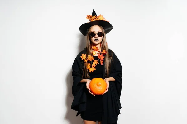 Une jeune fille gothique sexy célèbre Halloween, vêtue d'une sorcière, tient une citrouille dans ses mains — Photo