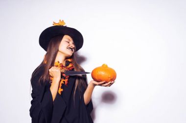 Gotik seksi Gotik kız Cadılar Bayramı, cadı, resimde kafasına sarı sonbahar yaprakları ile süslenmiş büyük bir siyah şapka kutluyor bir genç tutar bir kabak ve bir bıçak