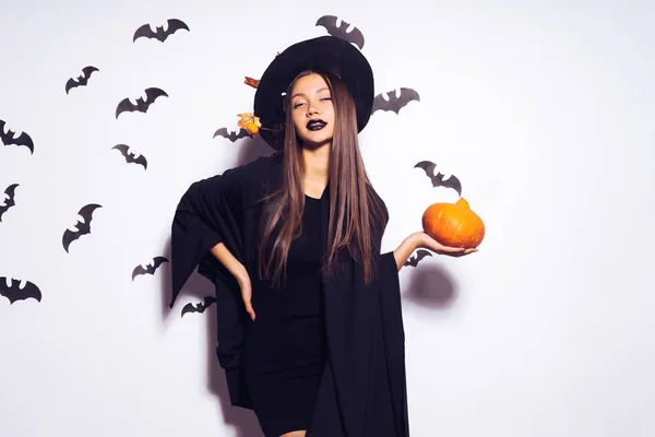 Ein junges gothic sexy gothic girl feiert halloween, im bild einer hexe, auf ihrem kopf trägt ein großer schwarzer hut, dekoriert mit gelben herbstblättern, einen kürbis in ihren händen — Stockfoto