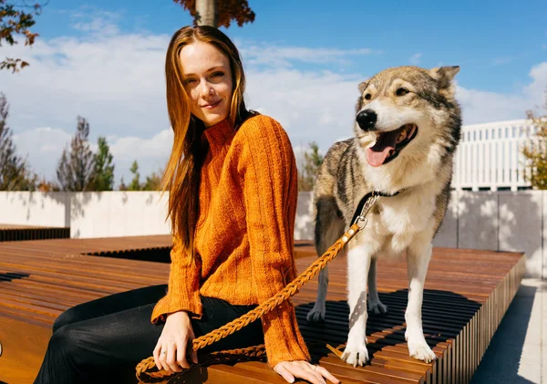Ung vacker rödhårig flicka i trendiga orange tröja promenader med sin hund i parken — Stockfoto