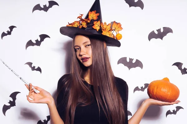 Una joven gótica sexy chica gótica celebra halloween, en la imagen de una bruja, en su cabeza un gran sombrero negro decorado con hojas amarillas de otoño sostiene una calabaza en sus manos —  Fotos de Stock