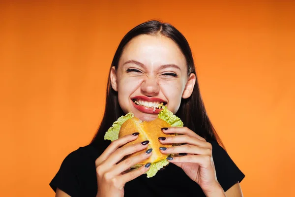 Молодая красивая девушка хочет похудеть, охотно ест вредный высококалорийный гамбургер — стоковое фото