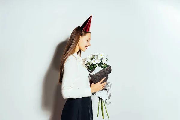 Una joven hermosa chica celebra algo, en su cabeza una gorra roja, sostiene un gran ramo de flores blancas en sus manos — Foto de Stock
