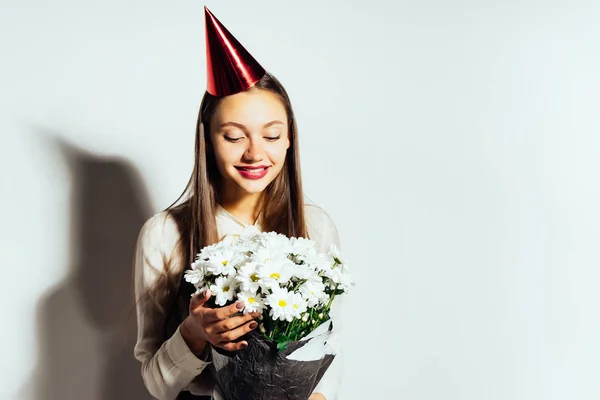 Uma jovem menina bonita celebra algo, em sua cabeça um boné vermelho, segure um grande buquê de flores brancas em suas mãos — Fotografia de Stock