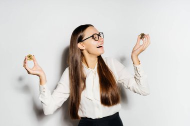 Beyaz bir gömlek ve gözlük genç modern bir başarılı kız altın bitcoins onun elinde tutuyor