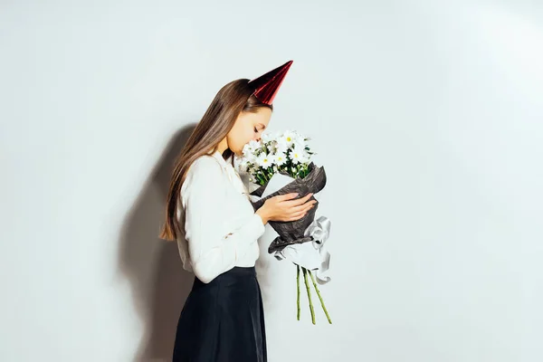 Gelukkig meisje vieren iets, het dragen van een pet, bezit een groot boeket van witte bloemen — Stockfoto