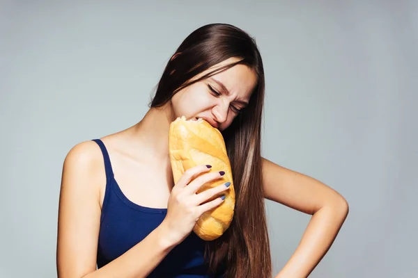 A young beautiful girl in a blue top wants to lose weight, holds in her hand and eats harmful white bread — Stock Photo, Image