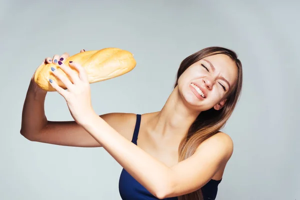 Молодая красивая девушка в голубом топе хочет сбросить вес, держит в руке и ест вредный белый хлеб — стоковое фото