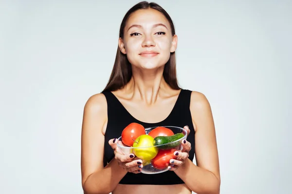 Молодая спортсменка в черном топе следит за своей фигурой, держит в руках тарелку с полезными овощами и фруктами — стоковое фото