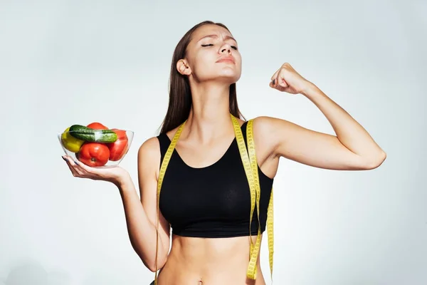 A young athletic girl in a black top keeps track of her figure, holds a plate with useful vegetables and fruits in her hands — Stock Photo, Image