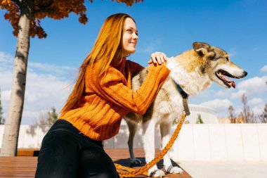 Onu köpek ile bir bankta oturan gülümseyen kız