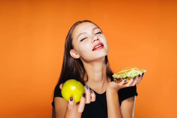 満足そうな表情で少女は、彼女の手でハンバーガーとリンゴを保持しています。 — ストック写真