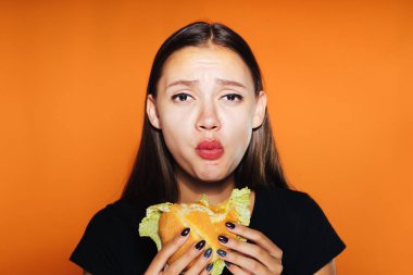 üzgün kız hamburger üzerinde turuncu bir arka plana sahiptir.