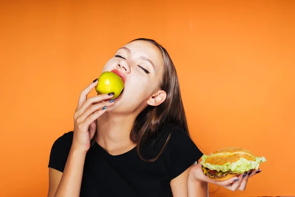 Girl on an orange background eating an apple — Stock Photo, Image