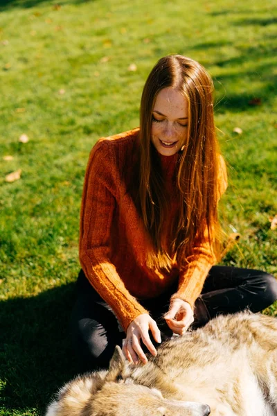 Flicka i en orange tröja sitter på gräset med sin hund — Stockfoto