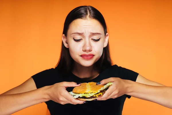 Rozrušená dívka držící burger na oranžové pozadí — Stock fotografie
