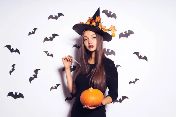 Krásná dívka fatální čarodějnice slaví halloween, zherzhit v rukou oranžové dýně a snaží se jí okouzlit s kouzelnou hůlkou — Stock fotografie