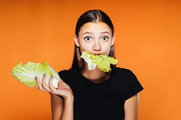 Güzel kız, kilo vermek istiyor bir genç yiyor bir sağlıklı düşük kalorili Pekin lahana, şaşırtıcı ve üzücü, arkasında görünüyor turuncu bir arka plan — Stok fotoğraf