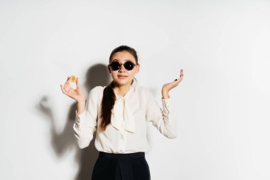 güneş gözlüğü ve beyaz bir gömlek kendine güvenen bir kız bir altın bitcoin onun elinde tutuyor ve şaşırır