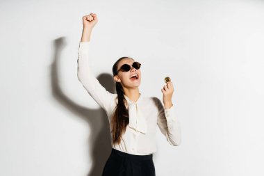 modern bir genç kız siyah güneş gözlüğü ve beyaz bir gömlek bir altın bitcoin onun elinde tutuyor ve mutludur, elini yukarı kaldırdı