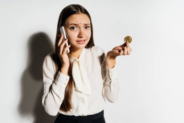 güzel bir başarılı kız kızgın görünüyor, kripto para birimi hakkında telefonda konuşuyor ve bir altın bitcoin elinde tutan
