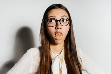garip bir modern kız gözlüklü bir altın bitcoin ağzına tutuyor