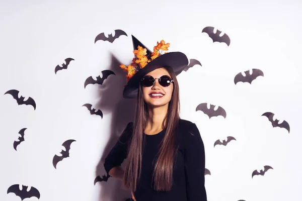 Schöne lachende Mädchen in Form einer Hexe zu Halloween, mit Sonnenbrille und einem großen schwarzen Hut posiert — Stockfoto