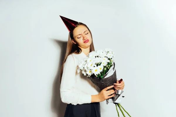 Funny cute girl in a white shirt is holding a bouquet of white flowers in her hands and looks displeased — Stock Photo, Image