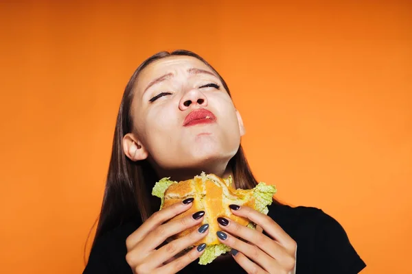 Smutná dívka chce zhubnout, ale jí škodlivé burger, za její oranžové pozadí — Stock fotografie