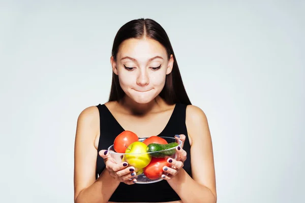 Una joven hermosa niña observa su peso, sostiene un plato con verduras útiles y frutas en sus manos, mira con curiosidad en su — Foto de Stock