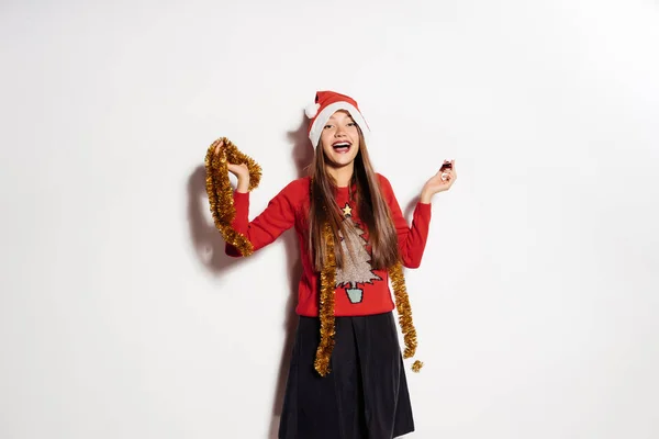 Ευτυχισμένη κοπέλα γιορτάζει το νέο έτος και τα Χριστούγεννα, σε ένα κόκκινο σκουφάκι, κρατά ένα χρυσό πούλιες — Φωτογραφία Αρχείου
