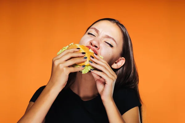 Молода дівчина хоче схуднути, але з нетерпінням їсть шкідливий бургер калорій — стокове фото