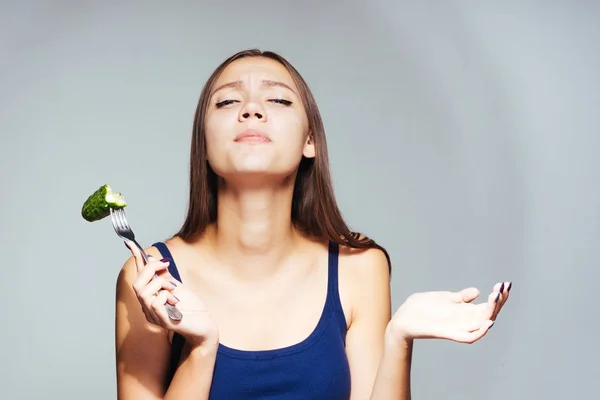 Schöne junge Mädchen in einem blauen Top sitzt auf einer Diät hält einen Stecker mit Gurke — Stockfoto