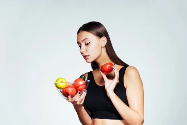 Bela menina de esportes sentado em uma dieta, segurando um prato com legumes e frutas e olhando para ela — Fotografia de Stock