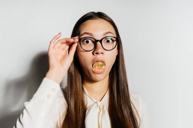 garip bir modern kız gözlüklü bir altın bitcoin ağzına koruyor ve şaşırmış görünüyor