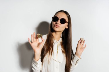 bir genç başarılı kız beyaz bir gömlek ve güneş gözlüğü altın bitcoin elinde tutan ve kendinden emin görünüyor