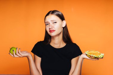 Siyah T-shirt bir genç güzel üzgün kız kilo vermek istiyor, onun elinde tutan yararlı bir elma ve zararlı bir burger ve değil seçebilirsiniz