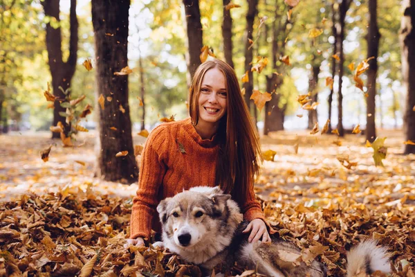 Bela rindo menina ruiva brincando com seu cão em folhas de outono caídas — Fotografia de Stock