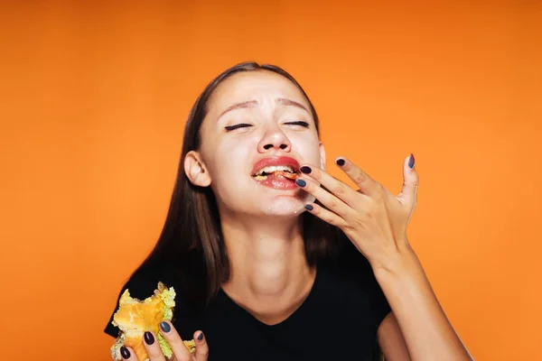 O ağırlığı izlemek değil çünkü turuncu bir arka plan üzerinde bir genç kız zararlı hamburger hevesle yiyor. — Stok fotoğraf