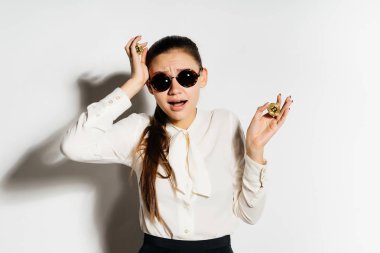 Beyaz bir gömlek ve güneş gözlüğü üzgün bir genç kız kafasına, onun elinde bir altın bitcoin tutunur