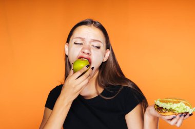 genç bir kız bir diyet oturur bu nedenle yararlı bir elma yiyor, zararlı hamburger elinde tutan