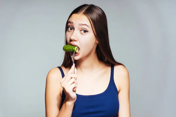 Молода дівчина на блакитному верху виглядає здивованою, сидить на дієті, тому їсть огірок низької якості — стокове фото